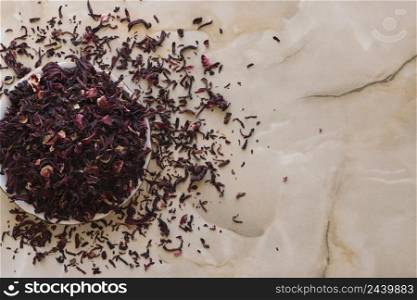 Dry hibiscus tea in a bowl. Dried hibiscus calyces, herbal tea made of crimson and deep magenta-colored sepals of the roselle flower, in the bowl on the table, top view.