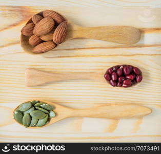 Dry ingredient of shelled almonds, adzuki red beans and pumpkin seeds in wooden spoon, top view on wooden table. Healthy food concept