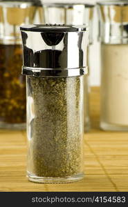 dry marjoram leaves in a glass jar on different spices background over wooden mat