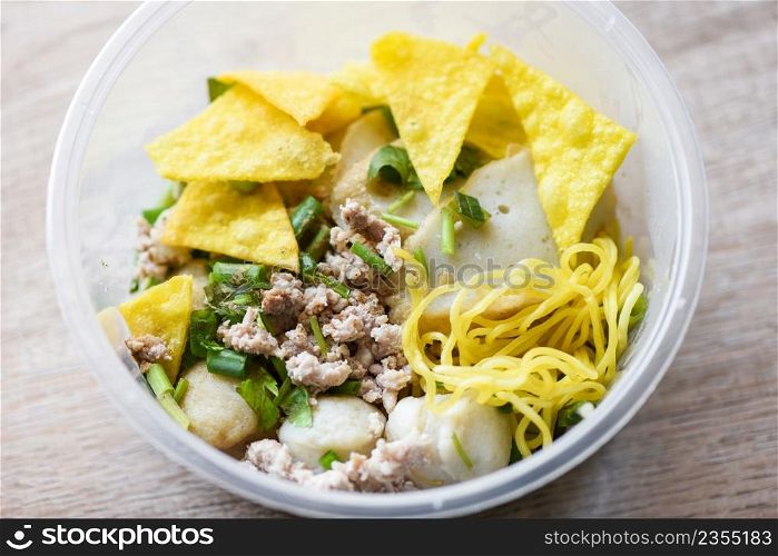 dry noodles pork balls fish balls and minced pork with crispy wontons and vegetable in plastic bowl on wooden table, top view Thai and China Asian food delivery concept