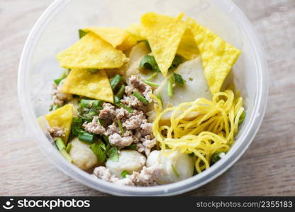 dry noodles pork balls fish balls and minced pork with crispy wontons and vegetable in plastic bowl on wooden table, top view Thai and China Asian food delivery concept