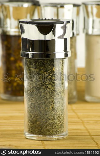 dry parsley in a glass jar on different spices background over wooden mat