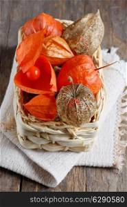 dry Physalis fruits in straw basket, isolated on old wooden background
