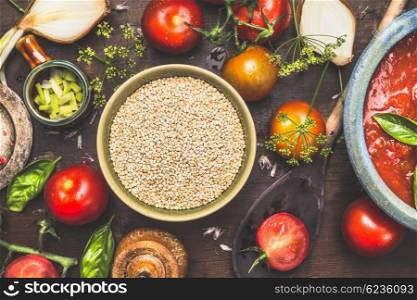 Dry quinoa with tomatoes and cutting vegetables ingredients, preparation on dark wooden background, top view. Quinoa cooking