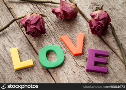 Dry roses with word LOVE on wooden background