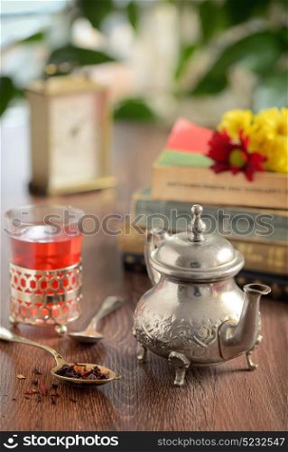 Dry tea leaves on spoon and teapot on wooden table