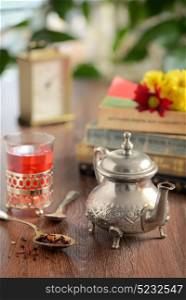Dry tea leaves on spoon and teapot on wooden table