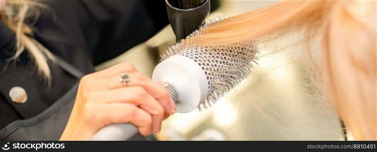 Drying straight blond hair with black hairdryer and white round brush in hairdresser salon, close up. Drying straight blond hair with black hairdryer and white round brush in hairdresser salon, close up.