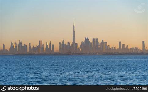 Dubai Downtown skyline with waves on sea beach, United Arab Emirates or UAE. Financial district in travel vacation concept. Urban city. Skyscrapers buildings with sunset sky.