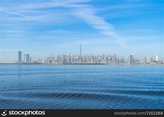Dubai Downtown skyline with waves on sea beach, United Arab Emirates or UAE. Financial district in travel vacation concept. Urban city. Skyscrapers buildings with blue sky. Reflection