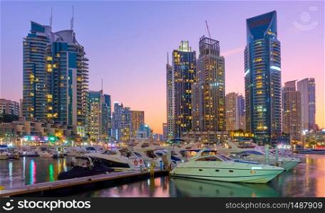 Dubai Marina at sunset - Illuminated modern residential towers and yachts in Dubai city in the evening, United Arab Emirates