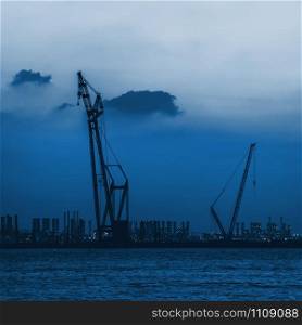 Dubai seaport, UAE. Silhouette of cranes on the sky background. Color of the year 2020 classic blue toned