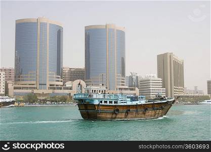 Dubai, UAE, A dhow, old wooden sailing vessel, cruises down Dubai Creek in front of the Rolex Tower.