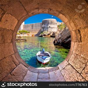 Dubrovnik small harbor under city walls view through stone carved window, famous tourist destination of Dalmatia