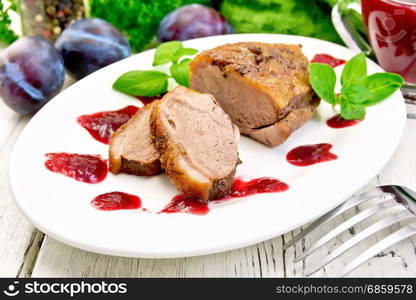 Duck breast with basil and plum sauce in a white oval plate against a light wooden board