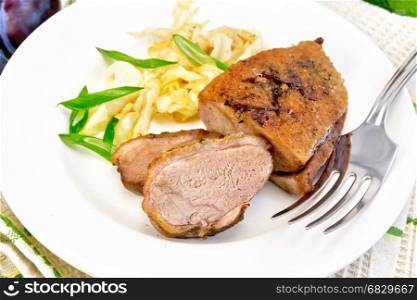 Duck breast with stewed cabbage and green onions in a white plate, fruits sauce, green towel on a wooden plank background