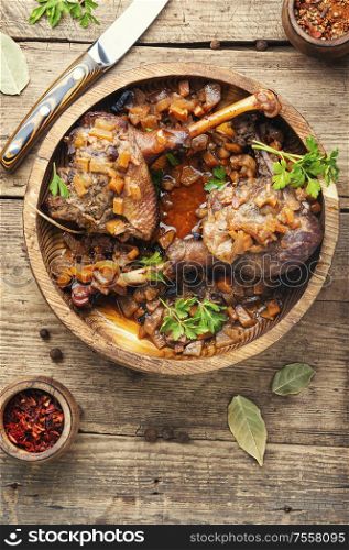 Duck legs baked with apple sauce in a wooden plate. Roasted duck leg with apple sauce