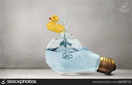 Duck toy. Glass light bulb and yellow rubber toy inside on blue background