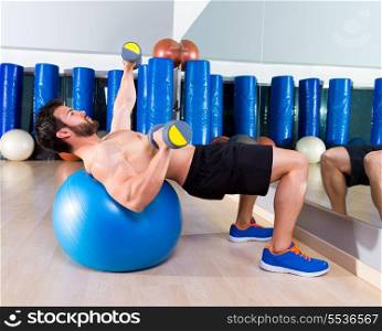 Dumbbell chest press on fit ball man workout at fitness gym