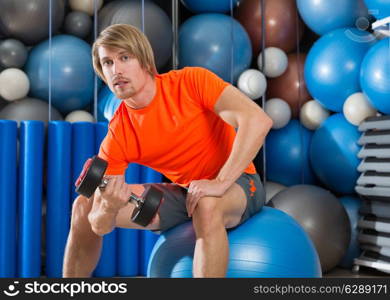 dumbbell concentrated biceps curl man workout at gym sit on swiss ball fitball