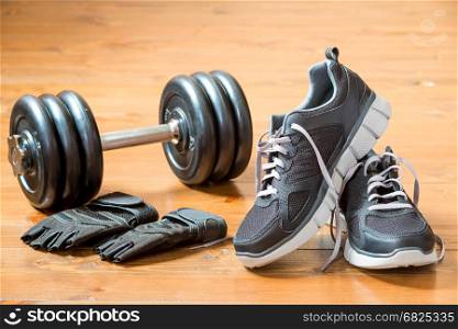 Dumbbells, gloves and sneakers in black on a dark wooden floor close-up