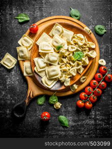 Dumpling and raw ravioli on a plate with tomatoes and spinach leaves. On dark rustic background. Dumpling and raw ravioli on a plate with tomatoes and spinach leaves.