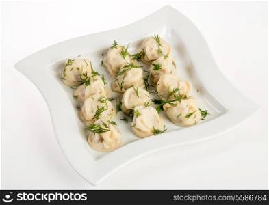 Dumplings (russian pelmeni - italian ravioli) with dill on a plate lying on a white background