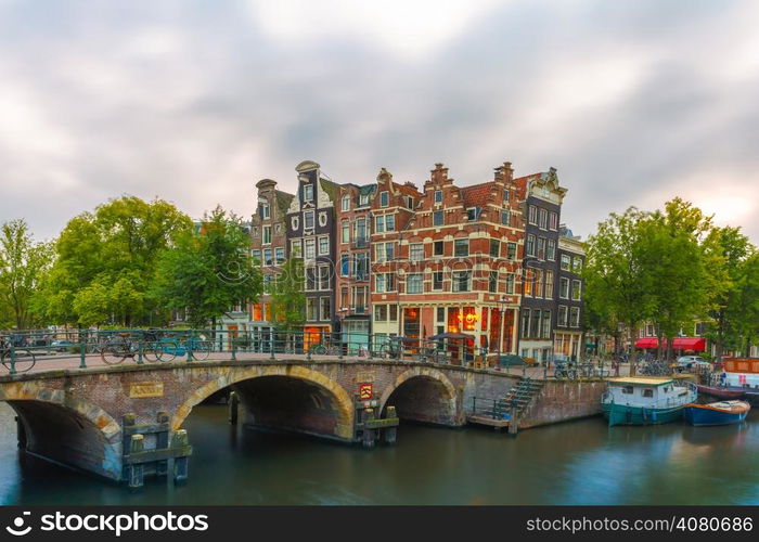 Dusk city view of Amsterdam canal, bridge and typical houses, boats and bicycles, Holland, Netherlands.