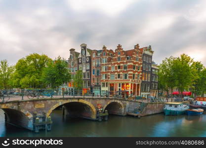 Dusk city view of Amsterdam canal, bridge and typical houses, boats and bicycles, Holland, Netherlands.