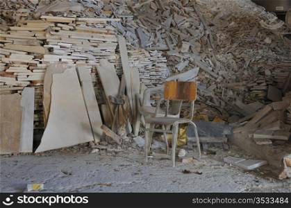 Dusty chair and pile of broken marble in abandoned factory interior.