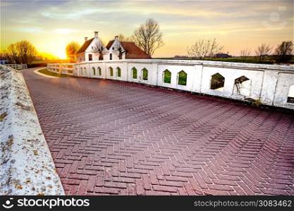 Dutch landscape with historical houses in evening along a curved road with white fence in the country - Groningen, Holland, Europe. Country road in dutch countryside with white fence leading towards an old farmhouse in Holland during an atmospheric sunset