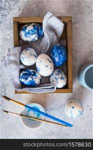 Dyed Easter eggs. ?lassic blue 2020 Easter eggs on the grey background. Blue speckled easter eggs with paint and brushes. Decorating eggs, preparing for Easter