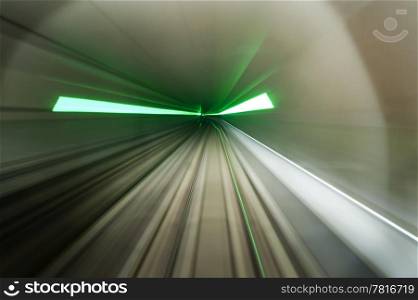 Dynamic image of a train, driving through a subway tunnel with green flares indicating emergency exits, lit by head lights.