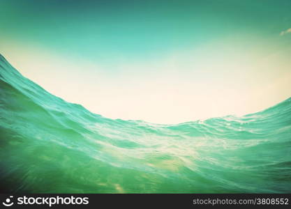 Dynamic water wave in the ocean. View from the waterline. Underwater and sunny sky. Vintage