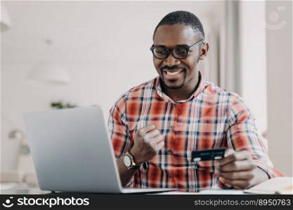 E-banking, e-commerce. African american man use e banking service at laptop. Black guy satisfied by easy secure payment, receiving benefits as loyal client, paying online, holding plastics credit card. E-banking, e-commerce. African american man holding credit card uses e-bank online service at laptop