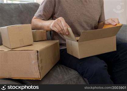 E-commerce concept parcel boxes made by cardboard was assembled with the clear tape by a man sitting on the sofa.