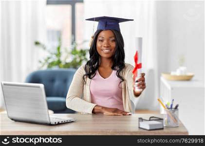 e-learning, education and people concept - happy smiling african american female graduate student with laptop computer and diploma at home. graduate student with laptop and diploma at home