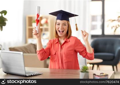 e-learning, education and people concept - happy smiling female graduate student in mortarboard with laptop computer and diploma celebrating success at home. student woman with laptop and diploma at home