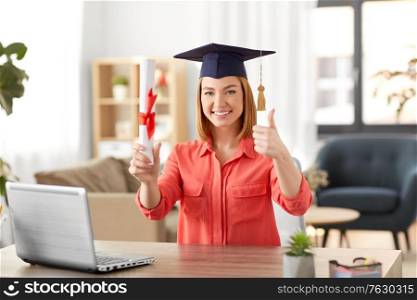 e-learning, education and people concept - happy smiling female graduate student in mortarboard with laptop computer and diploma showing thumbs up at home. student woman with laptop and diploma at home