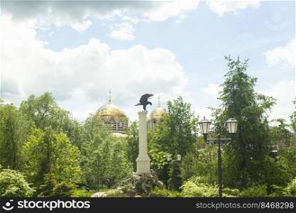 Eagle stone statue and Christian church with golden domes and cross in the Park.. Eagle stone statue and Christian church with golden domes and cross in the Park