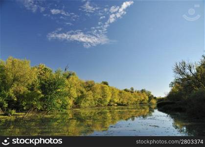 Early autumn sunny day by river with colorful trees reflection on water
