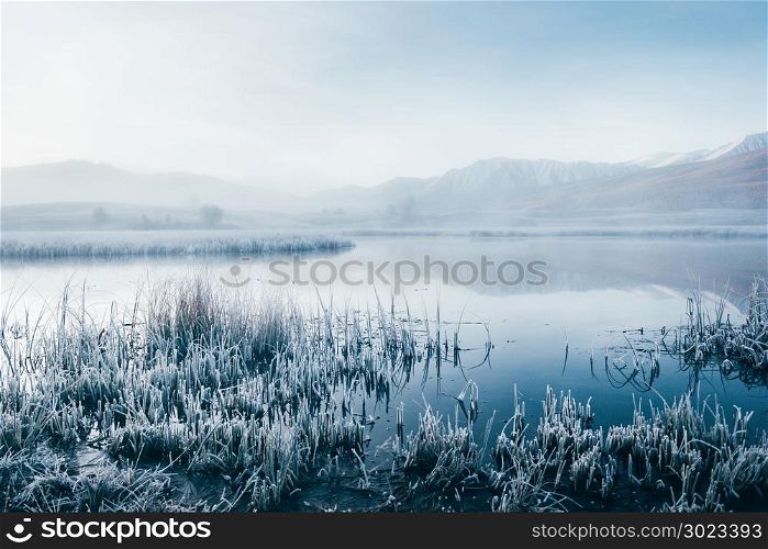 Early foggy morning on the shore of the lake mirror. Frost on the grass near the water.