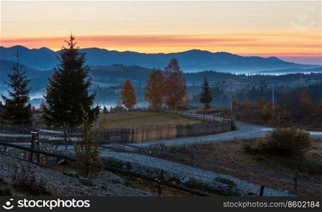 Early morning misty autumn slopes of Carpathian Mountains and rural road in mountain village  Yablunytsia village and pass, Ivano-Frankivsk oblast, Ukraine . Goverla and Petros mountains in far.