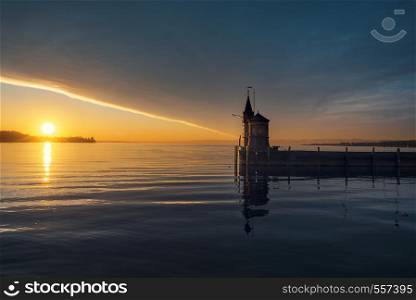 Early summer morning on lake Bodensee, Konstanz, Germany. Sunrise over water and lighthouse. Cloudscape and sun reflected on the water.