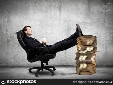 Earning money. Young confident businessman sitting in chair with legs on cent coin