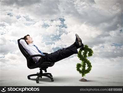 Earning money. Young confident businessman sitting in chair with legs on dollar sign