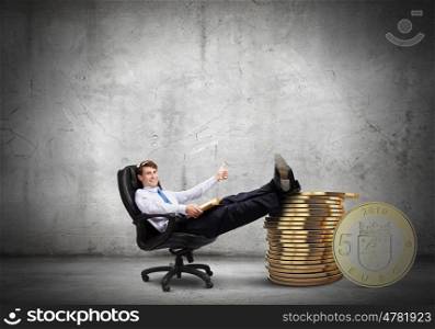 Earning money. Young confident businessman sitting in chair with legs on stack of coins