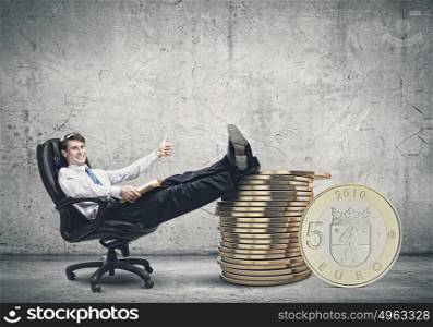 Earning money. Young confident businessman sitting in chair with legs on stack of coins