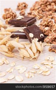 Ears of oat, flakes, granola and chocolate containing iron and dietary fiber, healthy snack or dessert concept. Ears of oat, flakes, granola and chocolate containing iron and fiber, healthy snack concept