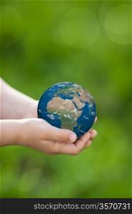Earth in children`s hands against green spring background. Elements of this image furnished by NASA